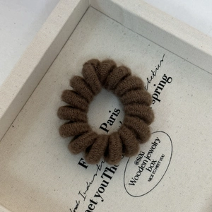 Detail view of a dark brown knitted spiral telephone cord hair tie on a beige tray