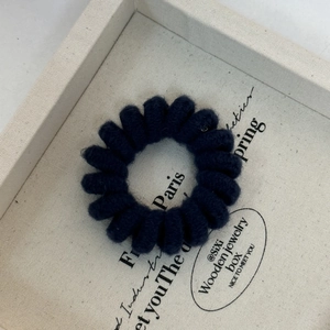 Detailed close-up of a navy blue spiral hair tie wrapped in soft yarn on a wooden tray