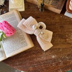 Detailed view of pink tweed bow hair claw clip with pearls on a vintage background