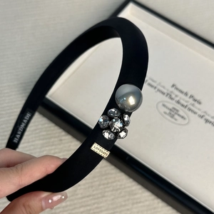 Detail of black satin headband featuring a grey pearl, crystals and a gold logo plate
