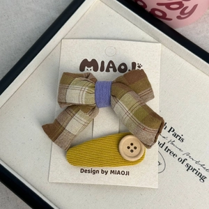 Détail d'un nœud à carreaux et d'une pince jaune à bouton en bois sur support carton