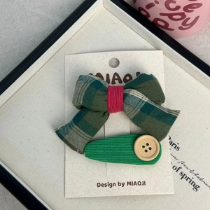 Détail du nœud papillon vert à carreaux et de la pince à cheveux en velours côtelé