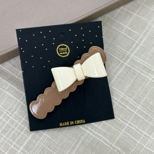 Détail d'une pince à cheveux avec nœud crème fait main sur une base café ondulée