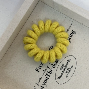 Detailed close-up of a bright yellow woven telephone cord hair tie on a display tray