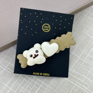 Détail de pinces à cheveux avec ours blanc et cœur sur base marron et carte noire