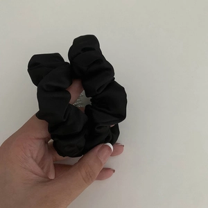Chouchou élégant en satin noir avec mini perles tenu sur un fond gris épuré