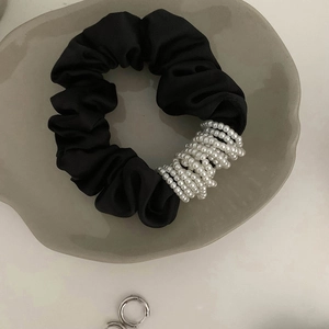 Détail du chouchou en satin noir orné de perles blanches dans un plateau gris