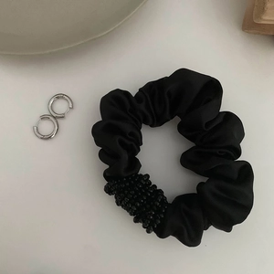 Vue détaillée d'un chouchou en satin noir perlé avec des boucles d'oreilles créoles en argent