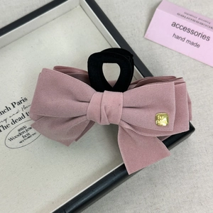 Detail view of pink velvet bow hair claw with gold fashion tag and black flocking