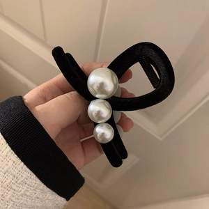 Detail of a large black velvet hair claw clip with pearls held in hand for size