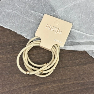 Détail d'élastiques à cheveux beige avec perles dorées sur support en carton de marque