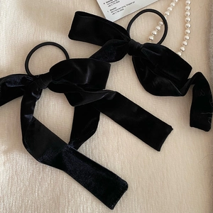 Two large black velvet bow hair scrunchies displayed with pearls on a textured background