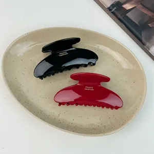 Elegant black and wine red acetate hair claws with gold logo on a ceramic plate
