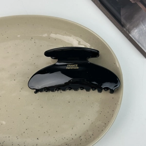 Close-up of glossy black acetate hair claw clip with gold France Handmade lettering