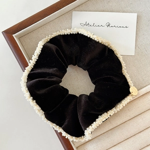 Detailed macro shot of black velvet scrunchie with faux pearls and handmade gold charm