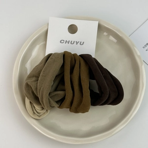 Close-up of four soft elastic hair scrunchies in earth tones on a ceramic plate