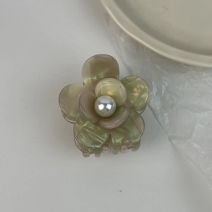 Vue détaillée d'une pince à cheveux fleur en acétate avec perle et reflets verts nacrés