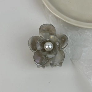 Détail d'une pince à cheveux en acétate gris fumé avec fleur et perle blanche au centre