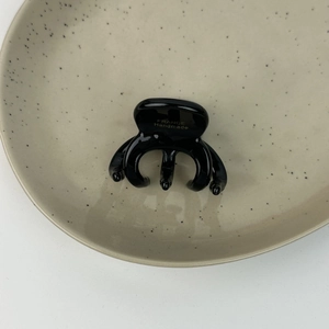 Détail de la pince à cheveux en acétate noir avec logo doré sur une assiette en céramique