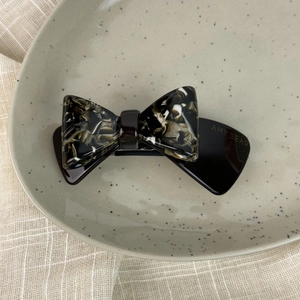 Detail of acetate double-layer bow hair clip with vintage marble pattern on a ceramic tray