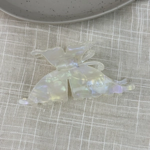 Detailed top view of a pearlescent butterfly hair claw clip with acetate texture on fabric