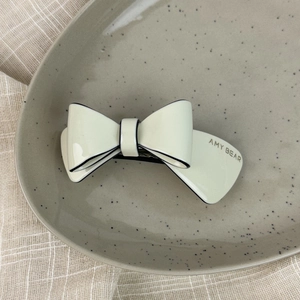 Detailed close-up of cream acetate double-layered bow hair clip on a textured fabric