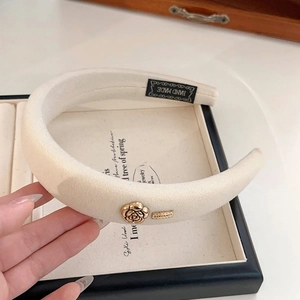 Detail of a beige velvet padded headband with a gold metal rose and LOVEDAYS metal tag
