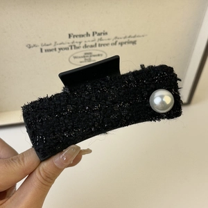 Detail view of tweed claw clip with large pearl accent and elegant black fabric texture
