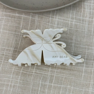 Detail view of cream marble butterfly hair claw with sawtooth grip and brand logo