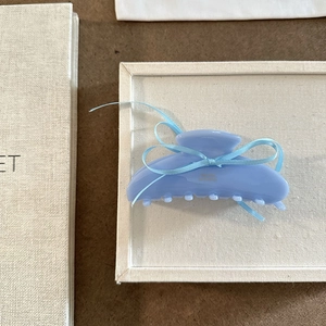 Dettaglio della pinza per capelli in acetato azzurro con fiocco e scritta dorata