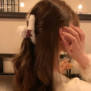 Close-up of white plush hair claw clip with red plaid bow worn on wavy brown hair