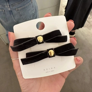 Detail of pair of black velvet bow hair clips with gold beads on display card