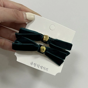 Close-up of a pair of dark green velvet bow hair clips with gold bead accents on a card