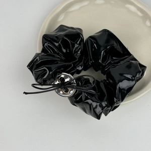 Détail d'un chouchou en cuir noir brillant avec bouton argenté et noeud sur plateau