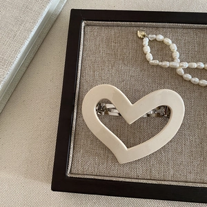 Detail of cream acetate heart hair clip with silver metal spring on wooden base