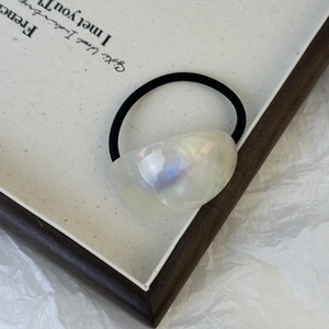 Detailed close-up of iridescent acetate hair tie with a minimalist cream white resin charm