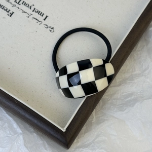 Detailed view of checkered acetate hair tie with black and white oval accent on canvas