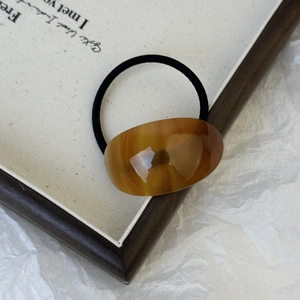 Detail showing amber resin oval piece on a black hair tie with natural swirl texture