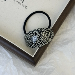 Detail of minimalist black and white cow print resin hair tie with elastic cord