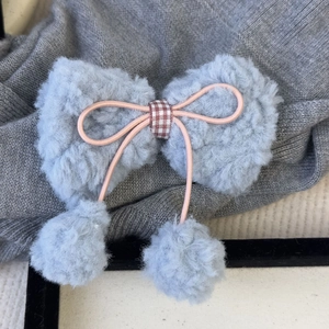 Barrette nœud en laine d'agneau crème avec pompons roses sur un fond de pull en tricot