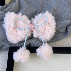 Détail de la pince à cheveux nœud rose en peluche avec pompons et ruban à carreaux