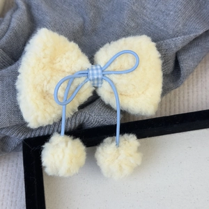 Détail de la barrette à nœud en laine d'agneau crème avec ruban bleu et pompons doux