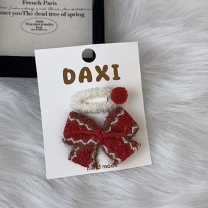 Close-up of a white plush BB clip and a red tweed bow hair clip set on a display card