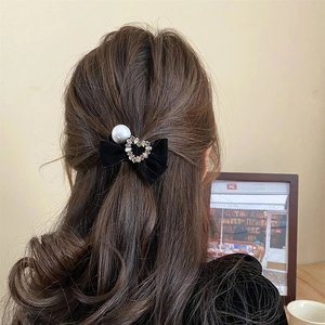 Detail van een zwarte fluwelen strik met strass hart en parel op golvend haar