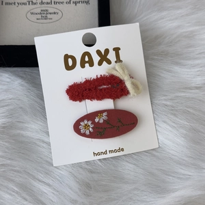 Detail of red plush hair clips with white bow and daisy embroidery on packaging card