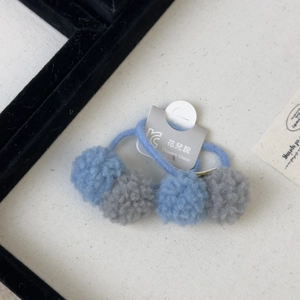 Close-up of dual plush pom-poms hair ties set in light blue and grey tones