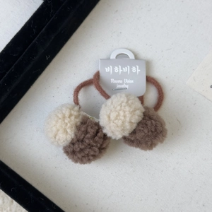 Detail of plush brown and cream pom pom hair clips with a grey display card