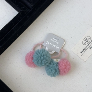 Detail of colorful woolen ball hair clips with pink and teal plush textures and elastic bands