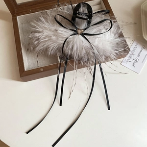 Vue macro d'une pince à cheveux en plumes avec nœud en soie noire et gemme en cœur
