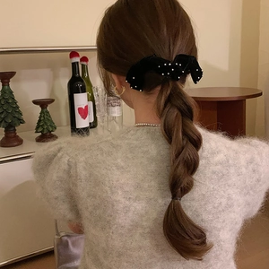 Close-up of black velvet bow hair clip with white pearls styled on a low ponytail